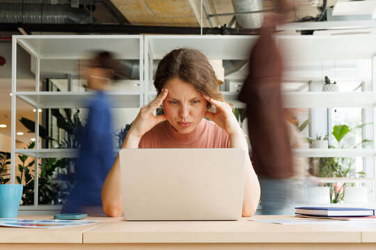 Stressed businesswoman works on laptop at busy office desk