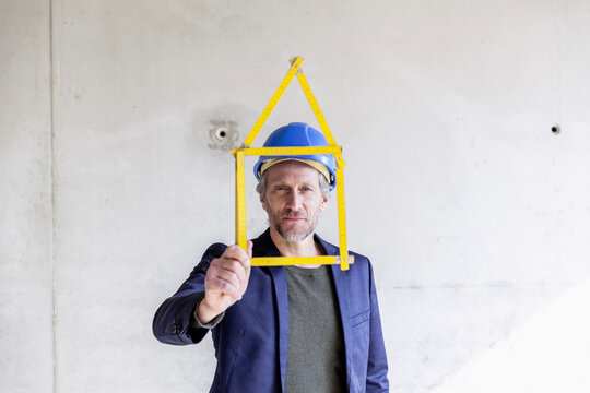 Man with hard hat holding pocket rule in shape of a house