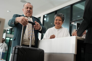 A senior traveller at the check in desk passes a boarding card over the counter beside the baggage drop of an airport, good for senior and business travel themes © ultramansk