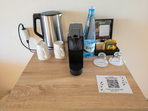 Modern hotel room coffee and tea station with electric kettle, espresso maker, water bottle, mugs, and QR code card