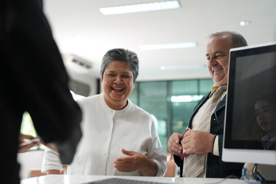 A mature couple at the airport desk react warmly to something the other said behind the glass of a departure hall counter, showing that travel connects people, both clearly in high spirits