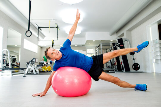 Senior man doing gymnastics on fitness ball in gym