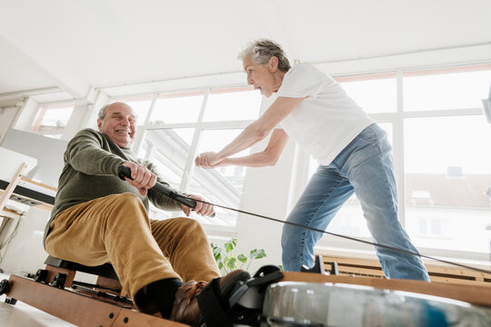 Woman cheers man using rowing machine indoors