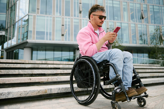 Man in wheelchair reads text message on smartphone in city
