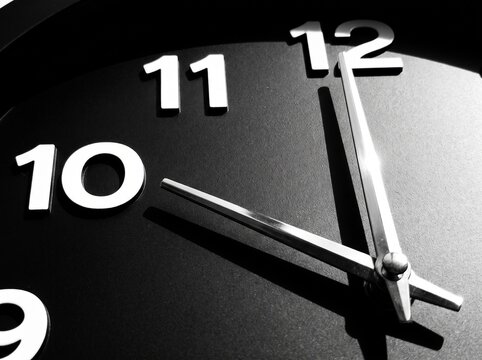 Black analog wall clock with white hour and minute hands showing time at 11:10