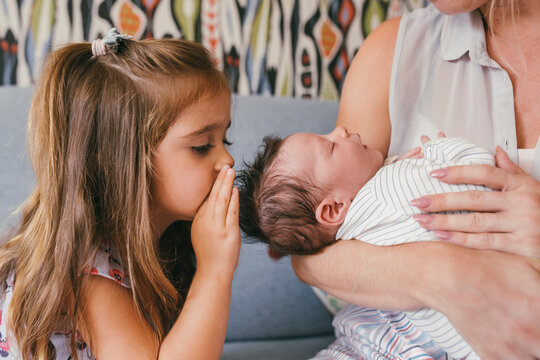 Mother holding her baby close with sister whispering at him