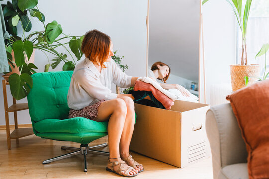 Happy woman sorts clothing into a cardboard box indoors