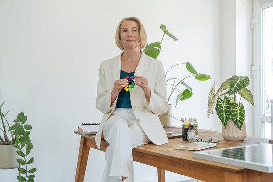 Senior businesswoman sitting on desk holding puzzle in office
