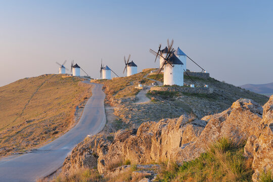 Row of windmills with rural road near Consuegra at sunrise