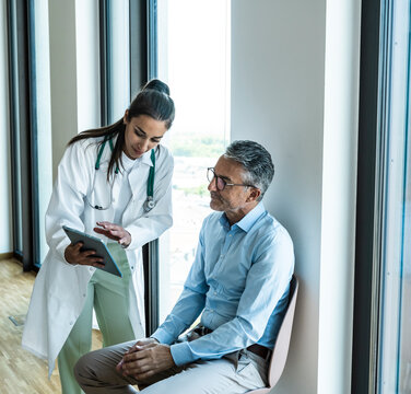 Woman doctor shows health advice on a tablet to a man in hospital