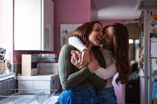 Lesbian couple embracing and smiling together in kitchen at home