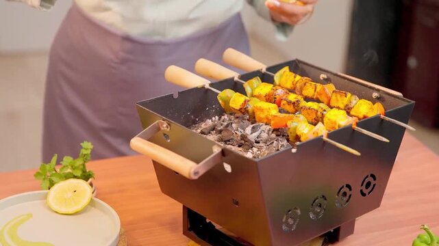 Person grilling paneer tikka skewers on a charcoal barbecue grill