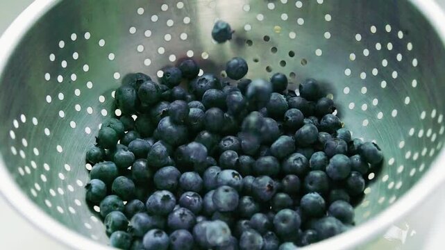 Fresh blueberries being washed in a metal colander for healthy food prep