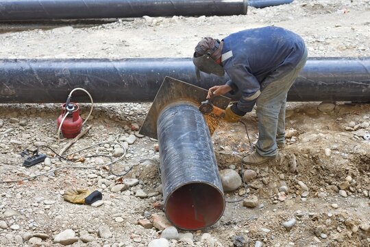 Professional laborer using angle grinder tool to cut steel pipe at utility construction site
