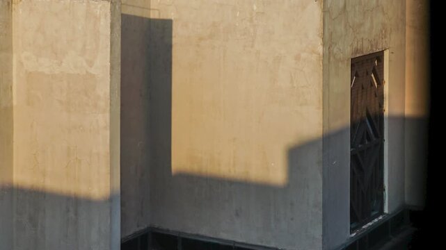 Sunlit plaster wall with geometric shadows and a dark metal gate