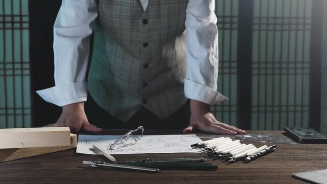 Architect in Plaid Vest Standing at Desk with Blueprints and Drafting Tools