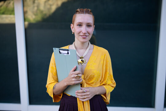 White woman holding clipboard wearing yellow top outdoors