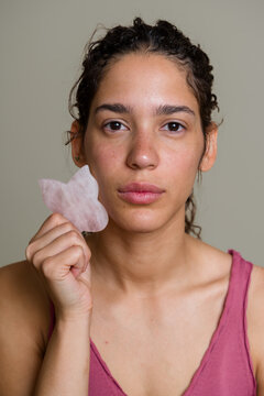 Hispanic woman using rose quartz gua sha facial massage tool
