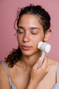 Hispanic woman using facial cleansing brush
