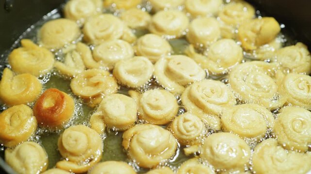 Sweet dough rosettes frying in hot oil inside a skillet close up background texture