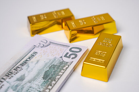 Three fine gold bullion bars arranged with two bars behind and one bar in front, placed next to a solid stack of United States fifty dollar bills.