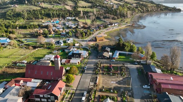Red-roofed houses and a wooden church cluster along the quiet streets of Curaco de V&eacute;lez, the tidal bay stretching behind this small, sunlit town on Chilo&eacute; Island, southern Chile.