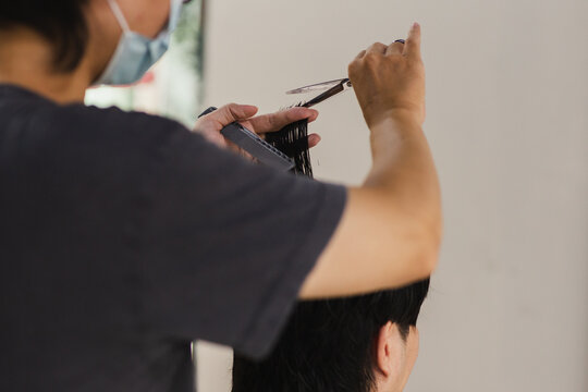 Close up of a professional hairdresser using scissors to trim client hair in salon.
