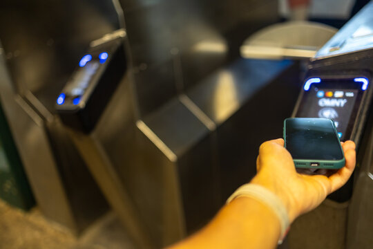 Hand holding a smartphone near a subway turnstile reader, using contactless payment technology for quick and efficient public transit access and fare payment