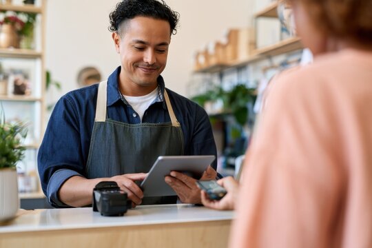 Customer makes a payment while shopkeeper uses a tablet for transaction in a retail store. Small Business Saturday