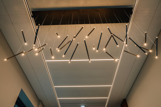 modern led ceiling installation with suspended linear lights and glowing bulbs, geometric arrangement against panels in an upscale contemporary interior architectural detail