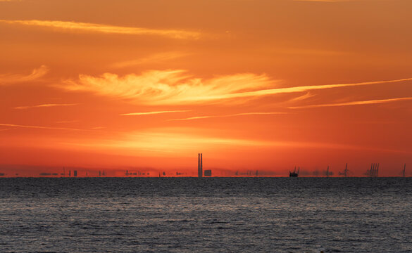 Luc-Sur-Mer, France - 08 08 2022:  Colorful sunrise over the sea and port of Le Havre far away