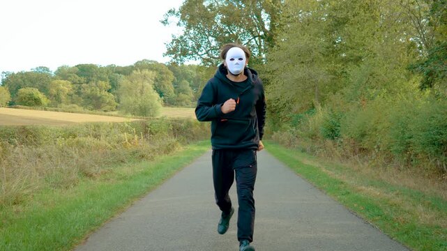 Masked attacker running toward camera on deserted country road, chasing victim and reaching forward to grab them. Criminal killer and murderer pursuit concept. Maniac, rapist, violent offender