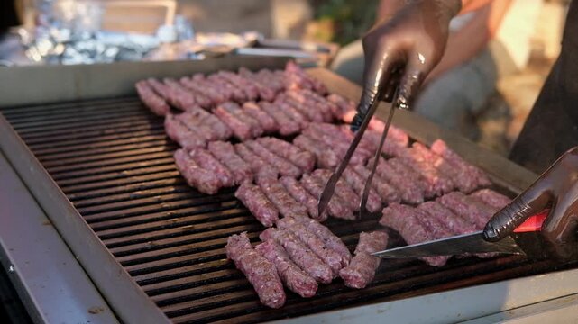 Traditional Balkan cevapi made from minced meat being grilled on a hot barbecue. Close-up of a cook preparing cevapi at an outdoor food stall