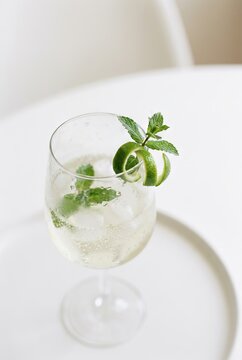 Refreshing cocktail with lime twist and mint in glass on white table