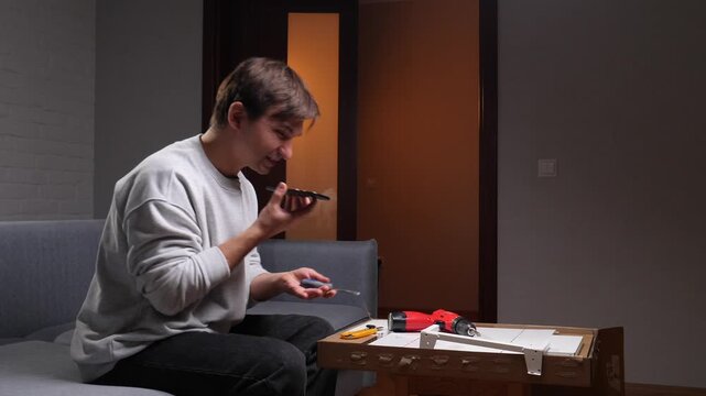 Man experiencing stress and frustration while struggling with home improvement, holding a phone to his ear and gesturing angrily at furniture parts, with tools spread on a box