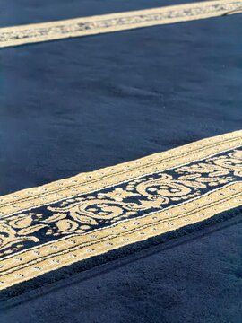 High angle shot of luxury dark navy Islamic rug showcasing intricate traditional golden ornaments, elegant prayer mat design background