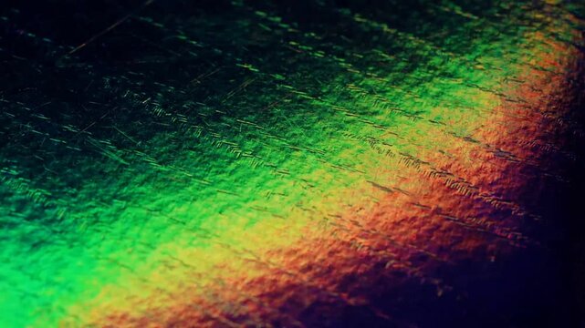 Dark oil-slick holographic foil with purple green and blue rainbow reflections flashing across micro-scratched metallic grain in a moody seamless loop