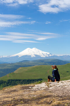 A female tourist sits on rocks and looks at Mount Elbrus in the North Caucasus