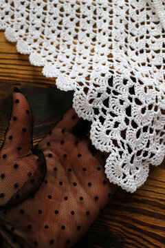 Elegant hand wearing a black polka dot mesh glove holding white handmade crocheted lace. Vintage delicate craft detail on dark rustic wooden surface. Perfect for fashion and craft design.