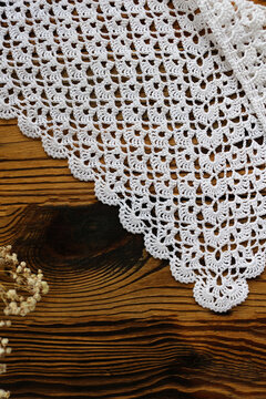 Delicate white handmade crochet lace kerchief scarf paired with gentle dried gypsophila flowers on a dark rustic wooden background. Romantic boho vintage fashion and lifestyle flat lay.