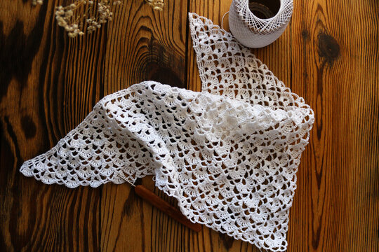 Delicate white handmade crochet lace kerchief scarf paired with gentle dried gypsophila flowers on a dark rustic wooden background. Romantic boho vintage fashion and lifestyle flat lay.