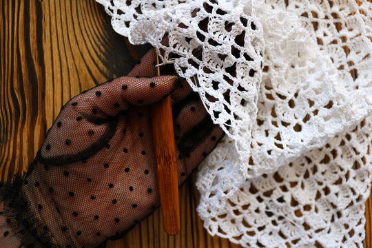 Elegant hand wearing a black polka dot mesh glove holding white handmade crocheted lace. Vintage delicate craft detail on dark rustic wooden surface. Perfect for fashion and craft design.