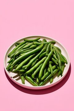 Fresh green beans piled on a white ceramic plate against a vibrant pink background with sharp shadows for healthy food blog and culinary marketing