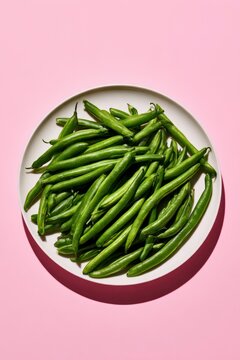 Fresh green beans on a white plate over a pink background in a minimalist top-down studio shot for healthy food blog and recipe marketing