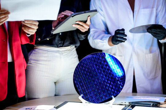 An engineer steadies the wafer under the bench light with the die pattern catching blue and violet across the surface inside a dimly lit research laboratory late in the working day