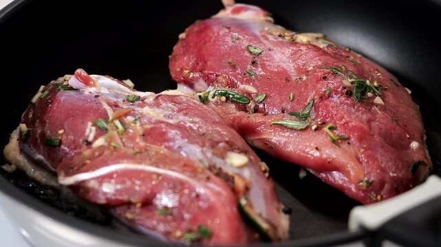 Close-up of raw duck breasts seasoned with rosemary, garlic and spices in a frying pan. Preparing marinated duck meat for cooking, gourmet dinner and homemade recipe.