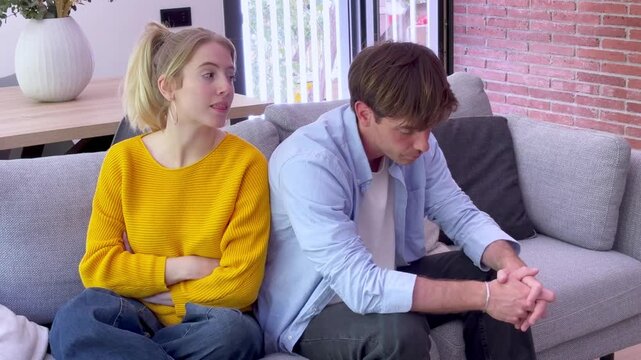 Young frustrated couple arguing and having relationship problems while sitting on the sofa at home, feeling angry and resentful after a difficult conversation in the living room