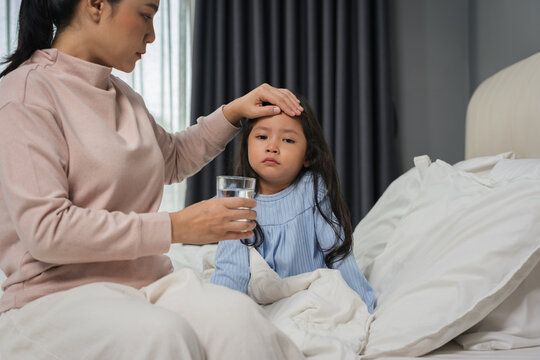 mother checking fever forehead and giving water to sick girl in bed