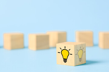 Wooden cube with glowing light bulb icon on blue background, representing creative idea, innovation, inspiration, problem solving, brainstorming, startup thinking, knowledge, and solution. © Keaw