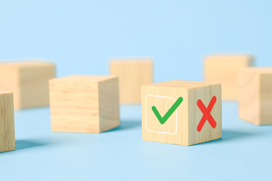 Wooden cube with green check mark and red cross on a blue background, representing right or wrong choice, approval, rejection, decision making, evaluation, voting, options, and selection.
